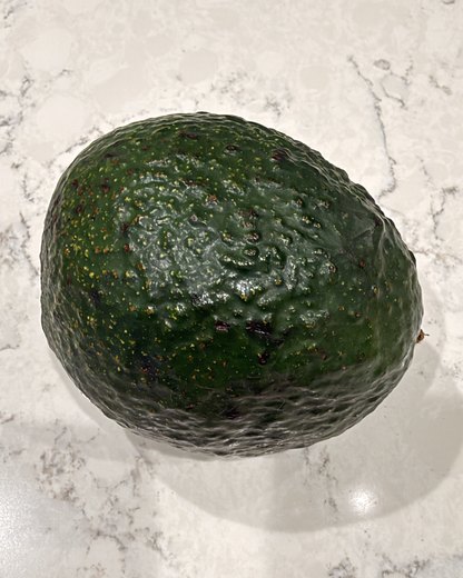A dark green avocado on a marble counter